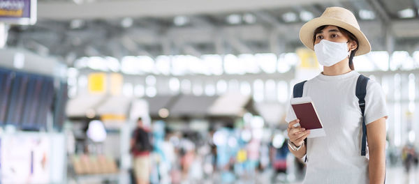 Woman wearing mask holding passport standing at airport