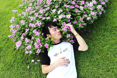 Man smelling pink flowering plants while lying on field