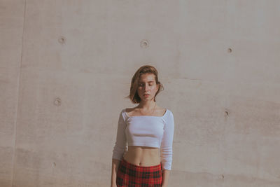 Portrait of young woman standing against wall