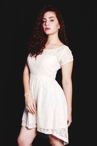 Portrait of young woman wearing dress against black background