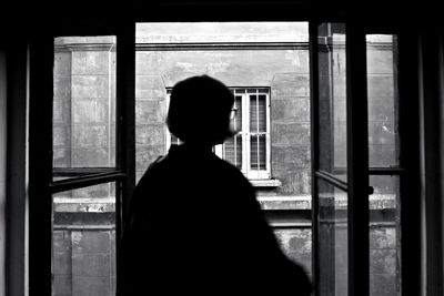 Rear view of silhouette woman looking through window
