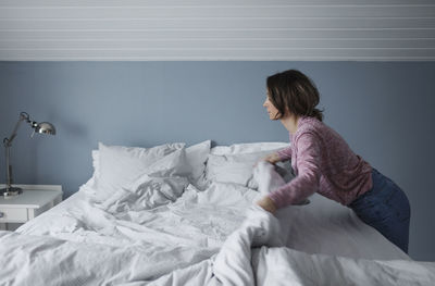 Side view of woman making bed at home