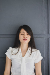 Young woman with eyes closed standing by wall