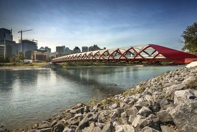 Bridge over river by buildings against sky