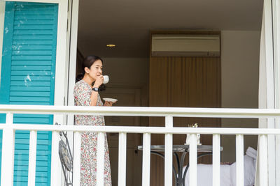 Woman drink coffee while standing against window of building