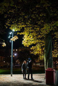 Rear view of friends walking on street against trees