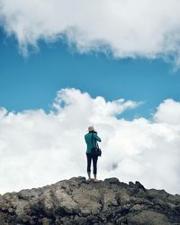 Rear view of woman standing on rock against sky