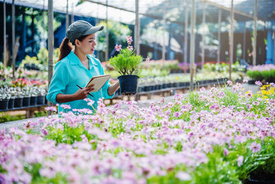 Woman holding flowering plants in greenhouse