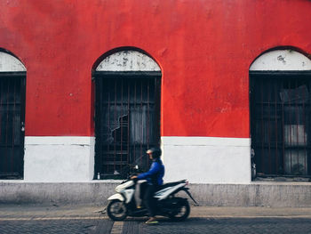 Side view of man riding motor scooter on street against building