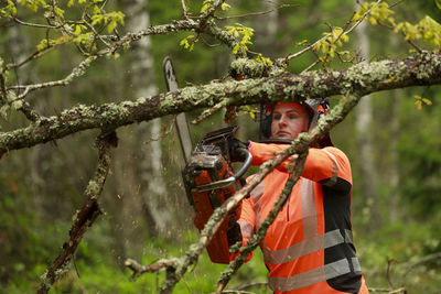 Female lumberjack cutting tree branch in forest