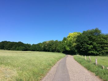 Road amidst field against clear blue sky