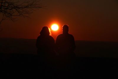 Silhouette of couple sitting against sky at sunset