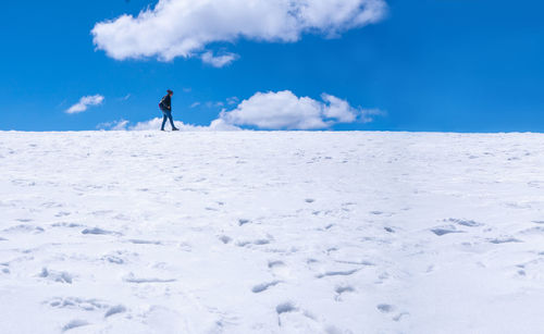Man on snow covered land against blue sky
