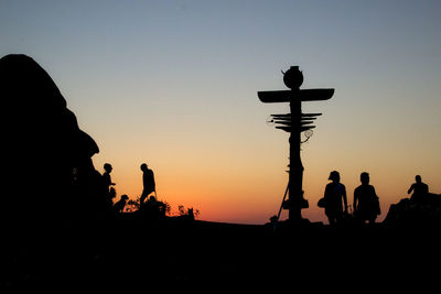 Silhouette people by cross clear sky during sunset