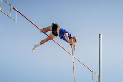 Low angle view of man climbing on pole against clear sky