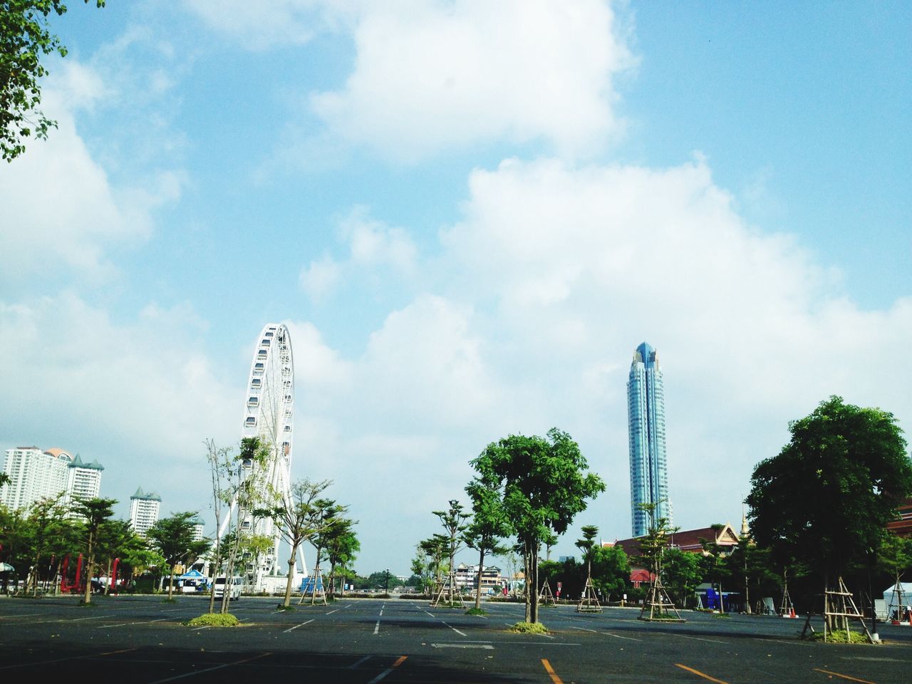 sky, tree, built structure, architecture, transportation, cloud - sky, road, low angle view, tall - high, city, cloud, land vehicle, ferris wheel, amusement park, day, building exterior, cloudy, travel destinations, blue, street