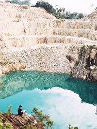 High angle view of man relaxing on rock formation by lake