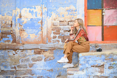 Side view of woman sitting against wall