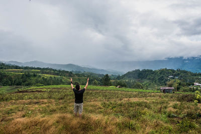 Rear view of man standing on field against sky