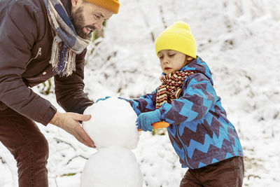 Father and son making snow man during winter