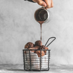 Close-up of hand pouring chocolate over donut holes churros on table against wall