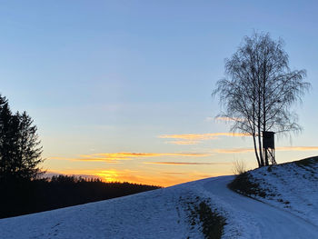 Snow covered field against sky during sunset