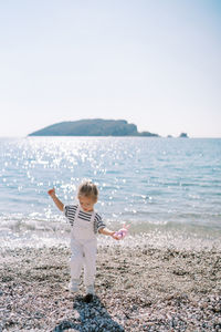 Full length of girl standing at beach against clear sky