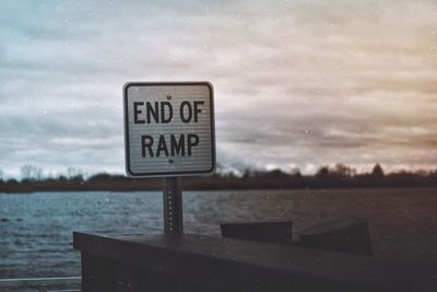 Close-up of road sign by sea against sky
