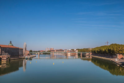 Bridge over river by buildings against blue sky