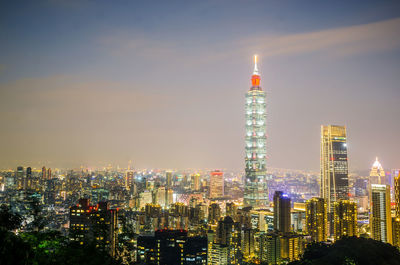 Illuminated modern buildings in city against sky at night