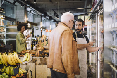 Mature retail clerk pointing while talking with senior male customer at grocery store