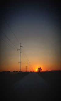 Silhouette electricity pylons on road against sky during sunset