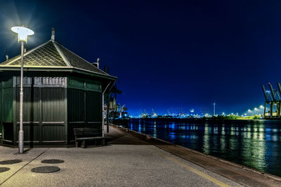 Illuminated building by river against sky at night