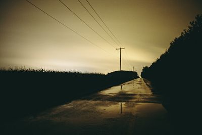 Silhouette electricity pylon by road against sky during sunset