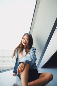 Portrait of smiling young woman sitting against window