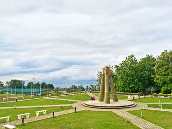 Trees on grassy field against cloudy sky
