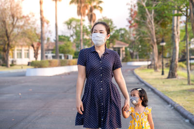 Mother and daughter wearing medical face mask prevent flu, pollution and covid 19 walking at street.