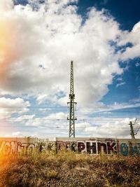 Electricity pylon on field against cloudy sky