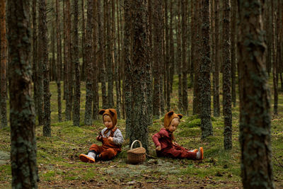 Toddler baby twins in bear bonnets sitting in the woods