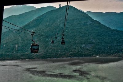 Overhead cable cars over mountains against sky