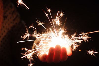Cropped image of person holding lit sparkler at night