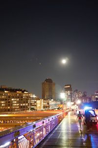 Illuminated street amidst buildings against sky at night