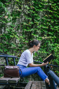 Young woman using mobile phone while sitting on tree