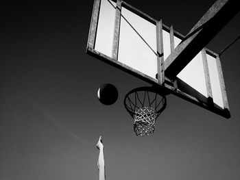 Cropped hand throwing ball in basketball hoop against sky