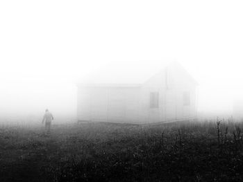 Man standing on field by building against sky