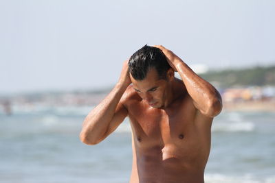 Close-up of shirtless man standing at beach against sky