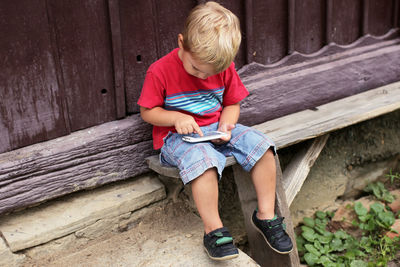 Full length of boy sitting on wooden wall