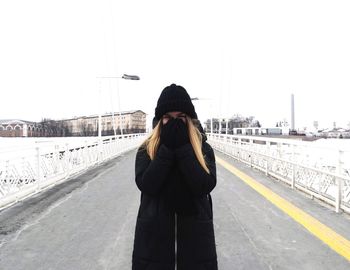Portrait of woman with hands covering mouth standing on bridge in city