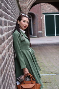 Portrait of woman standing against brick wall in city