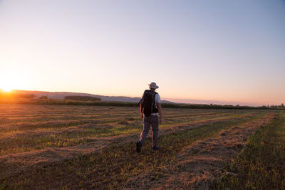 Rear view of man walking on grass against sky during sunset